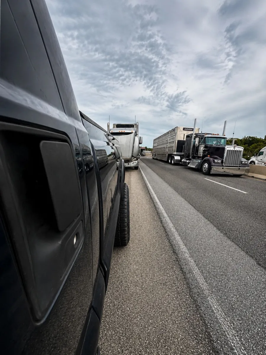 Pickup parked on the shoulder of a highway as semis roll past