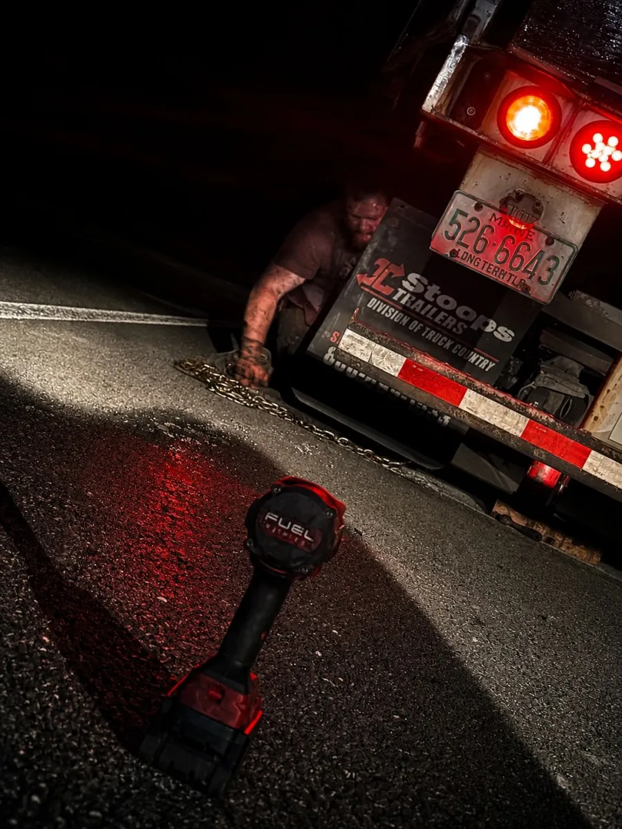 Mechanic working under the rear of a flatbed trailer at night